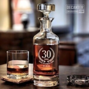Personalized Wellington lead-free crystal whiskey decanter with custom engraved Wreath laurel emblem design, shown with matching whiskey glass.